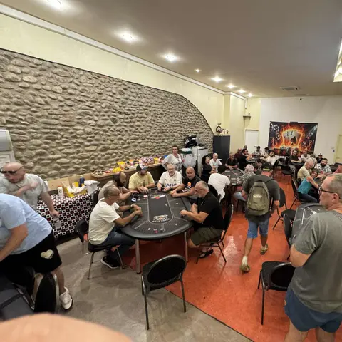 La grande salle du club un soir de tournoi : plusieurs tables pleines, le mur en galets et le plan de table projeté au mur.